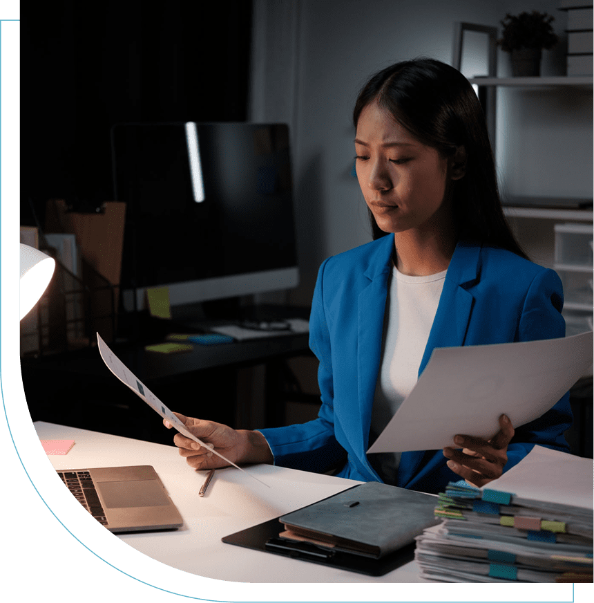 A woman working late at her desk with documents and a computer.