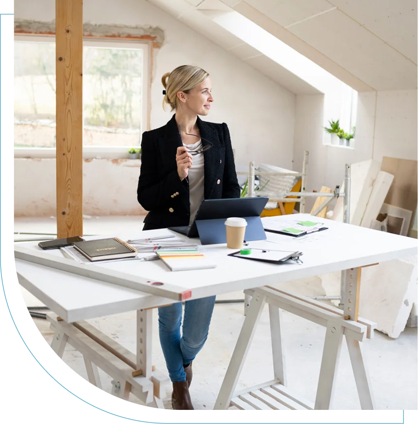 Woman working on a laptop in a bright, modern office with architectural plans.