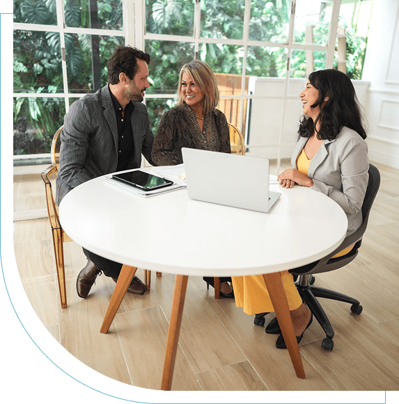 Three people discussing work around a white table in a bright office.