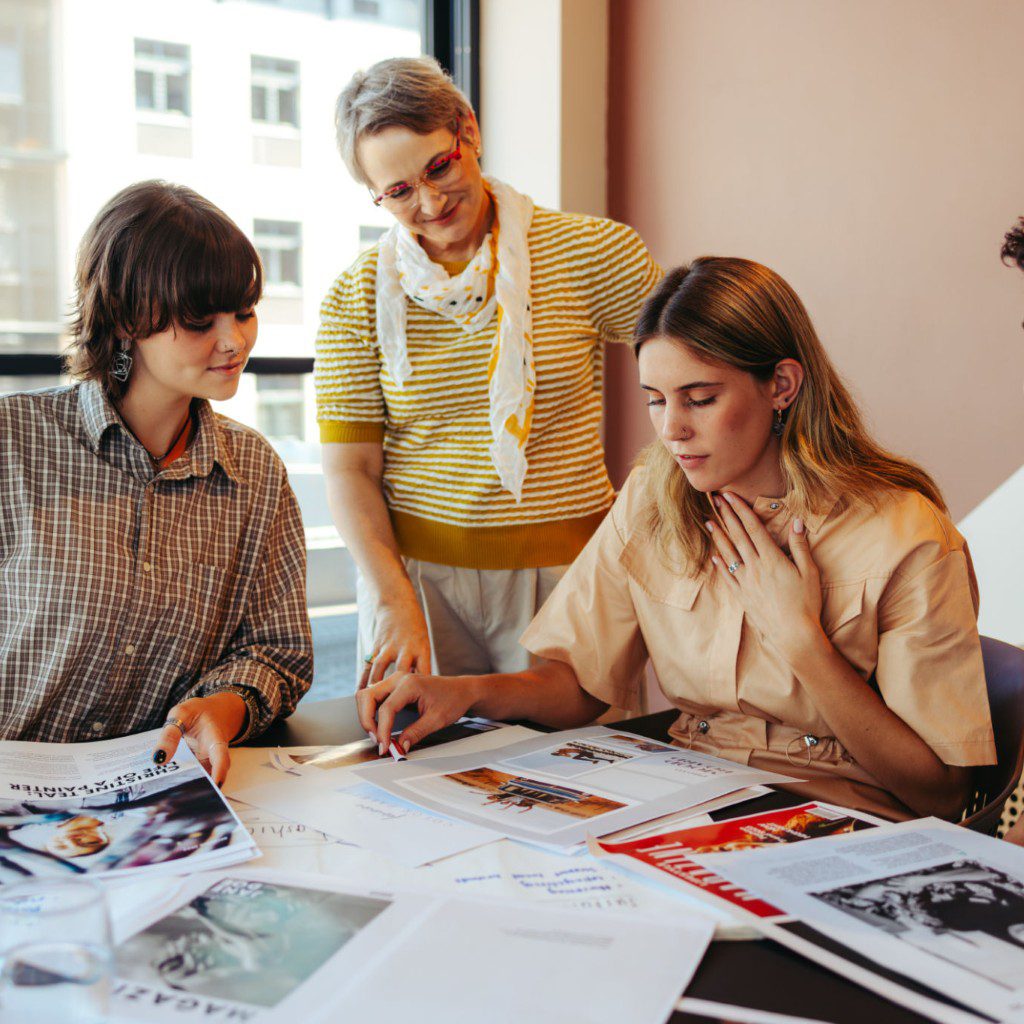 Three young adults collaborating over creative work at a desk.